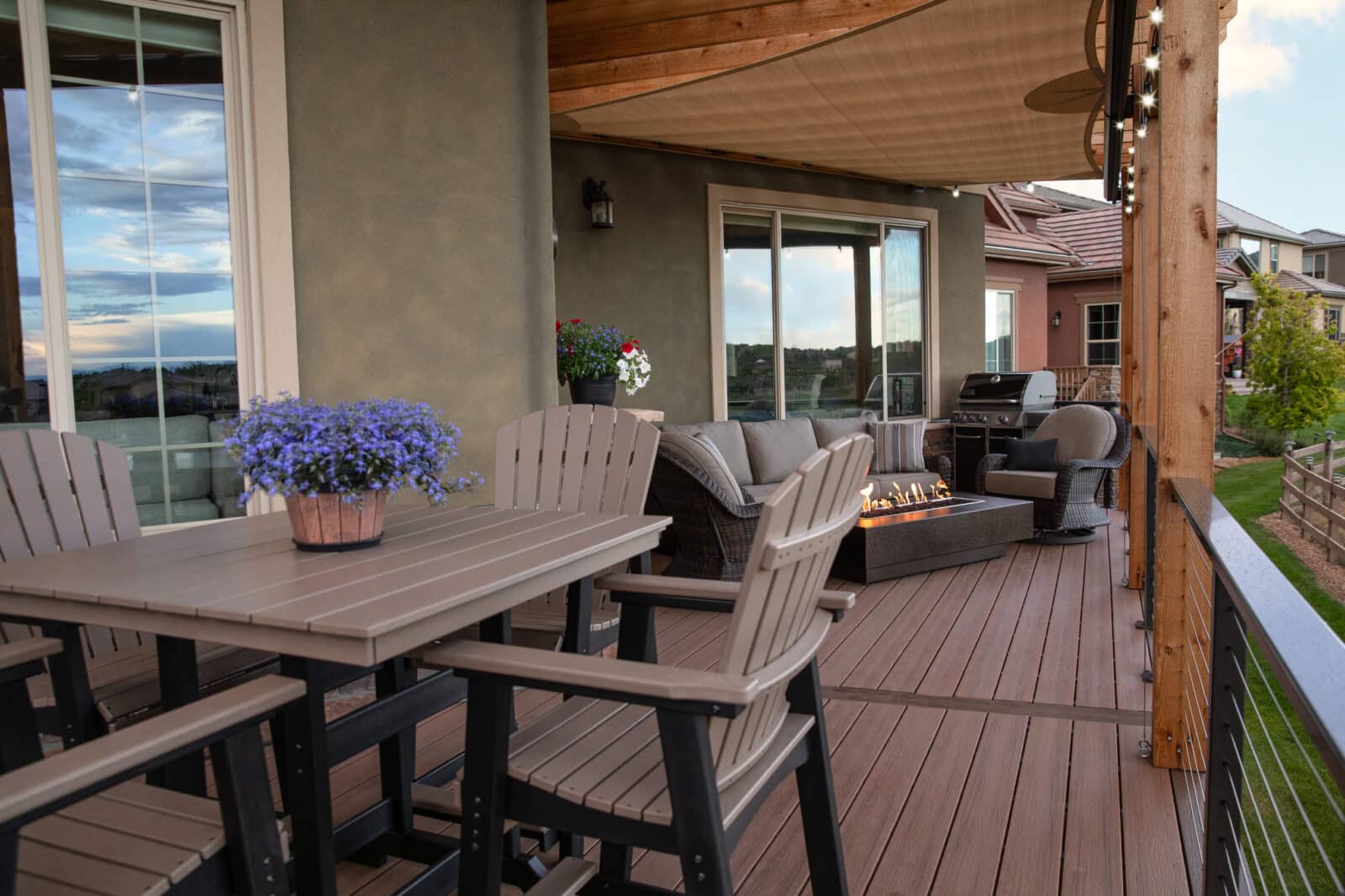 Composite deck with outdoor dining set, fire pit seating area, grill station, and a shade sail for comfort.