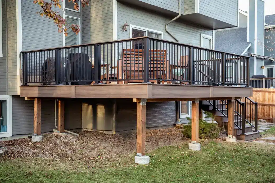 Elevated composite deck with black metal railings, wood support posts, and an outdoor dining area.