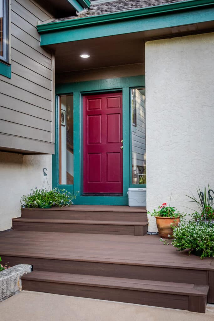 Front entrance with composite decking steps, a bold red door, and decorative potted plants