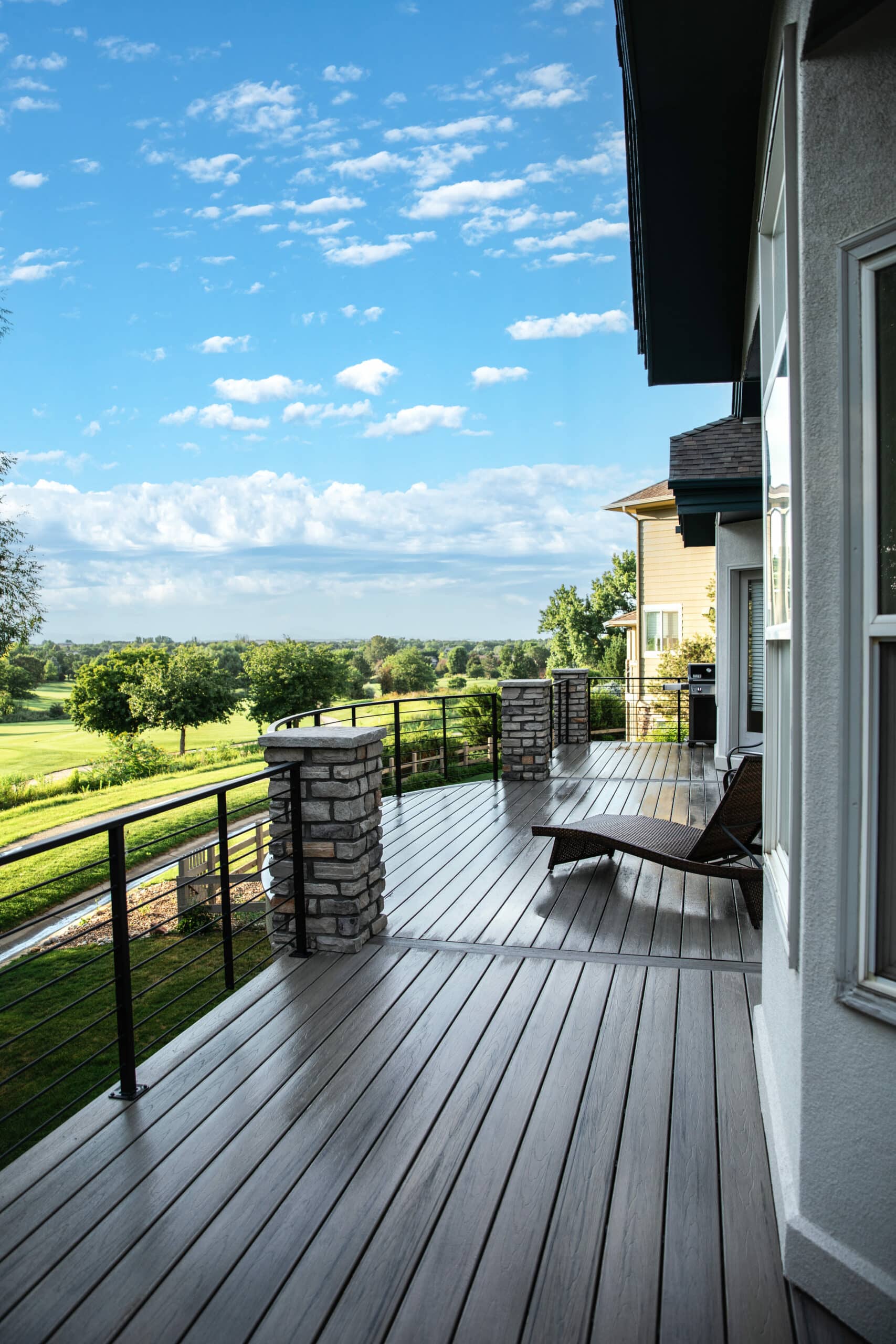 composite deck with curved boards, stone columns, and cable railing.