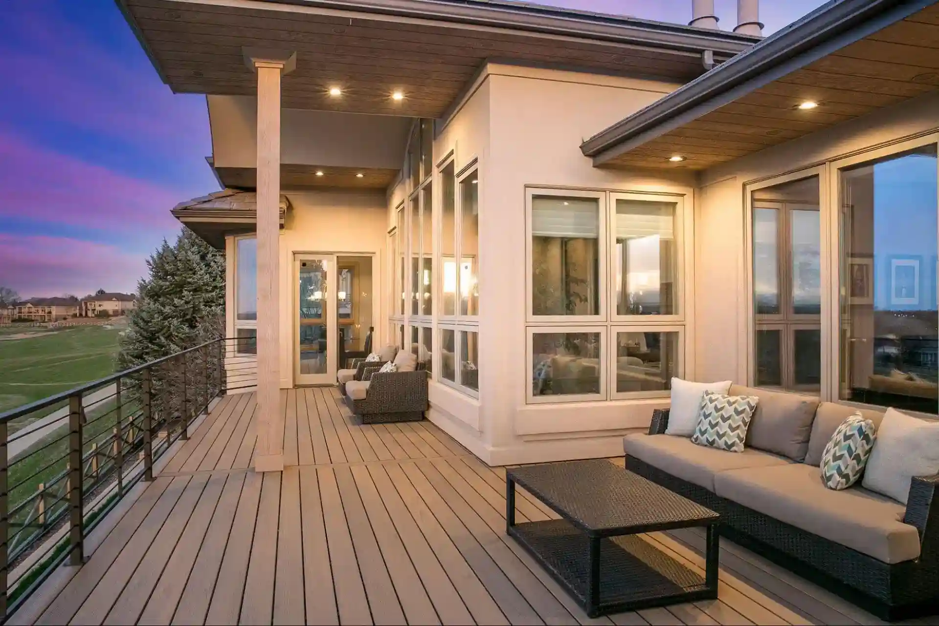 Spacious composite deck with modern outdoor furniture, cable railing, and warm lighting, overlooking a scenic sunset view.
