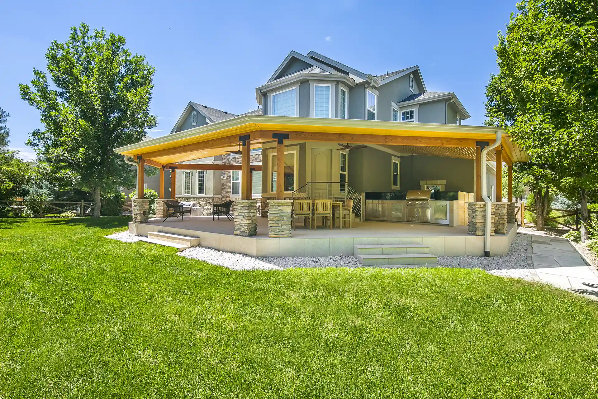 A covered outdoor deck with seating and an outdoor kitchen are attached to a two-story home.