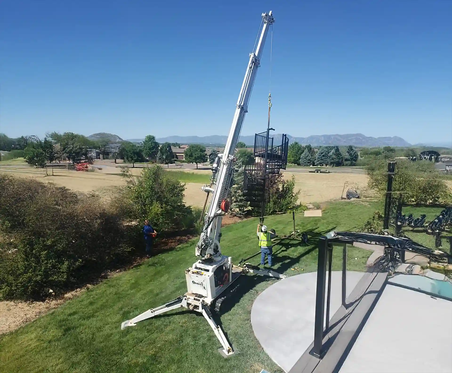 Crane lifting a metal staircase for deck installation.