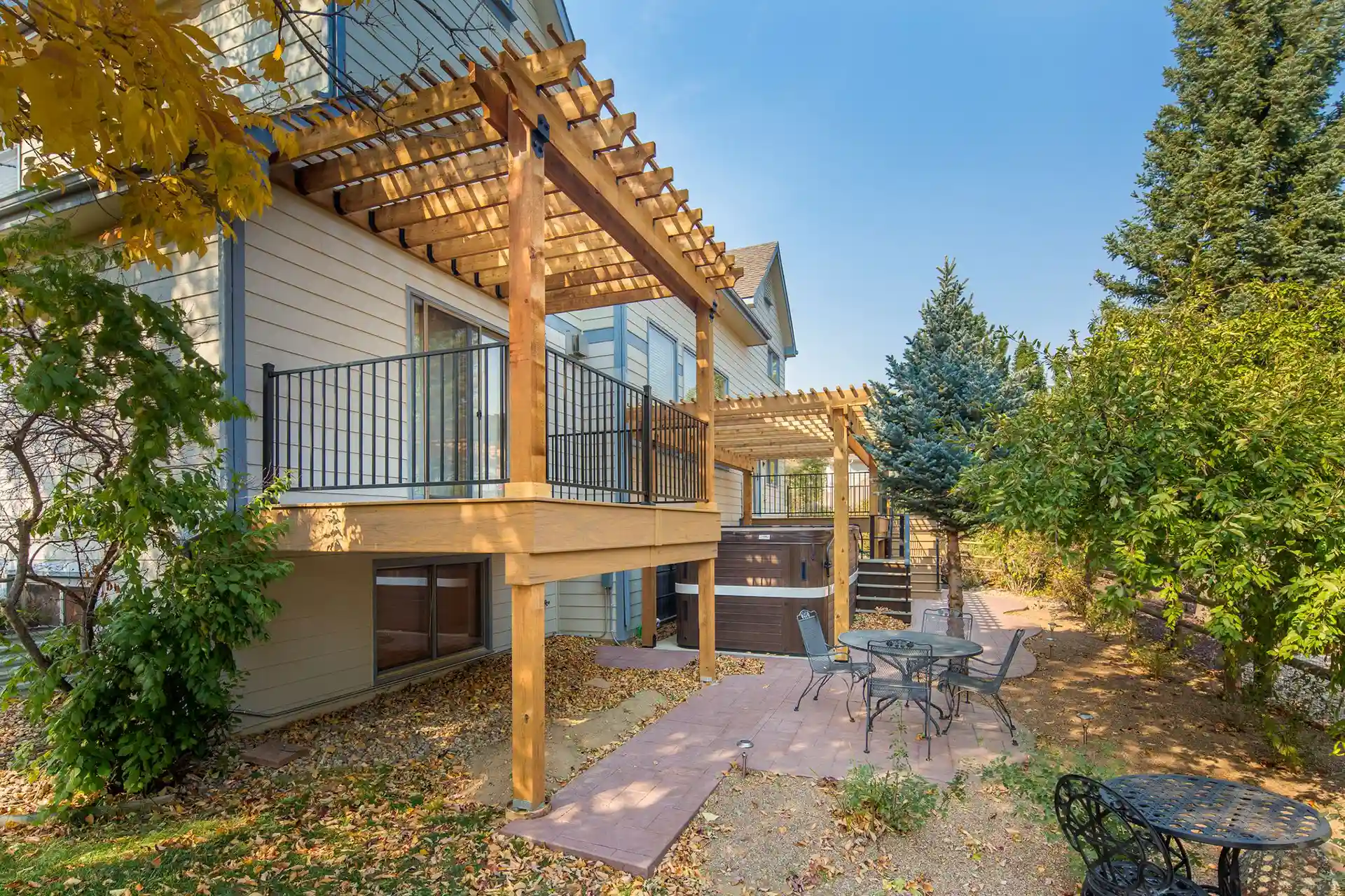 Multi-level deck attached to a home, featuring wooden pergolas for shade, metal railings for safety, and a patio area below with outdoor seating.