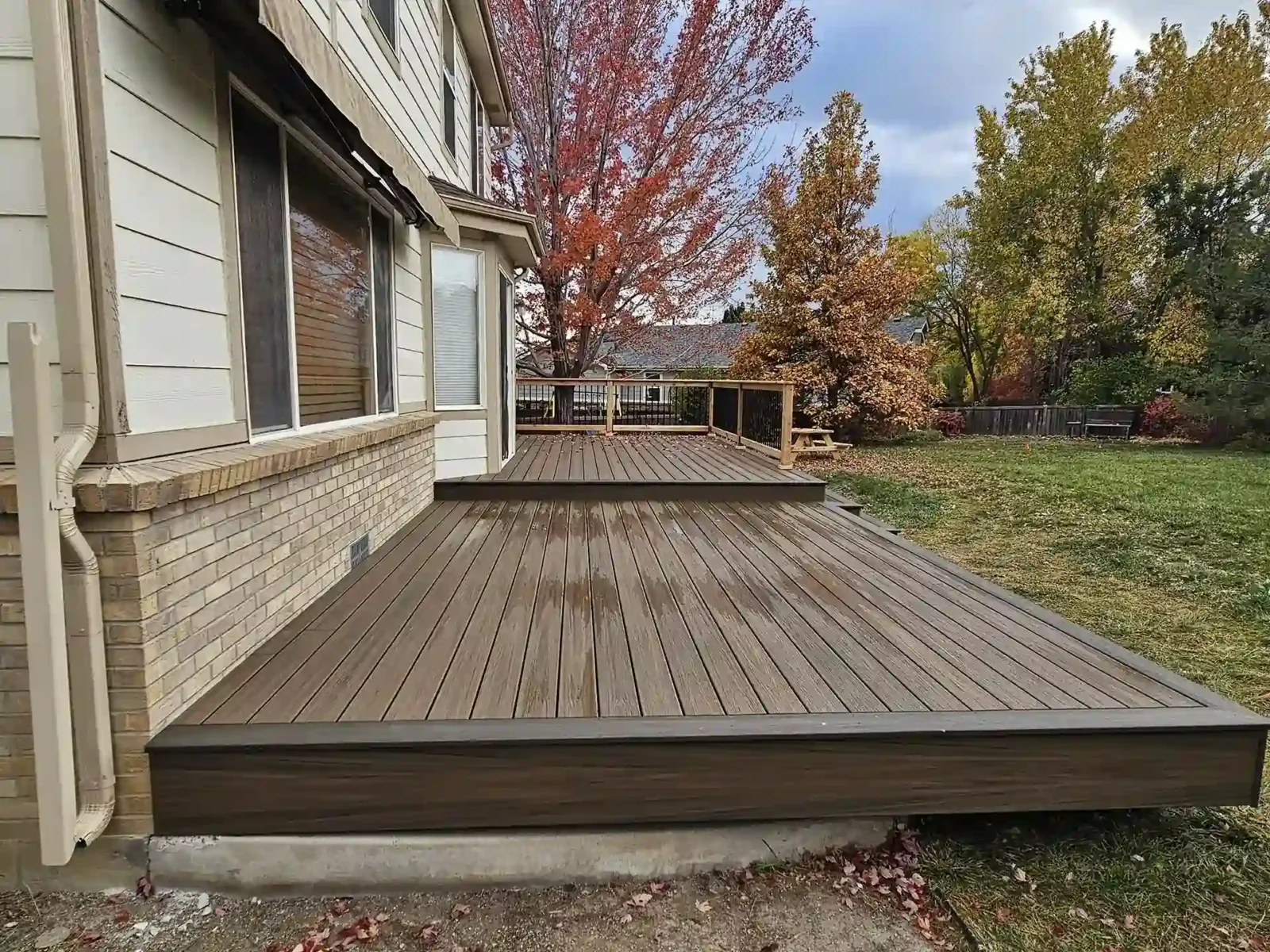 Two-tiered composite deck attached to a home, featuring a modern design, overlooking a spacious backyard with trees and greenery.
