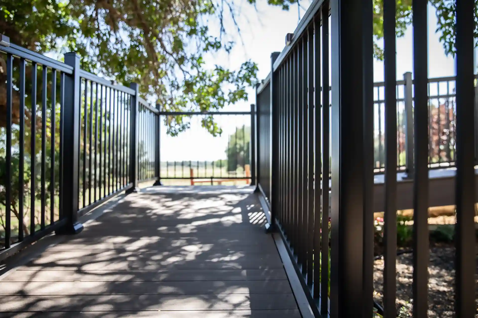 Close-up view of a deck with black metal railings casting shadows on the wooden floor, surrounded by trees and greenery in the background. 