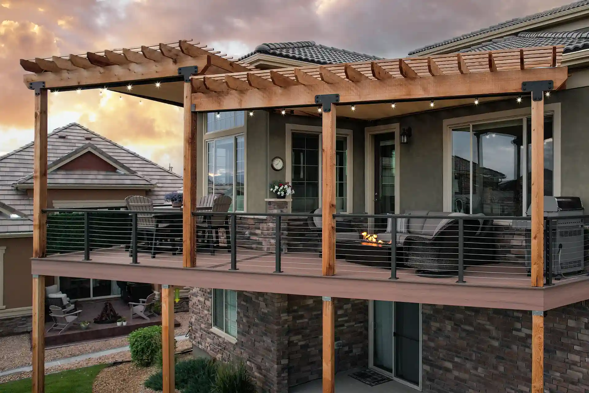 A modern wooden deck with a pergola overhead, featuring metal railings with horizontal cables.
