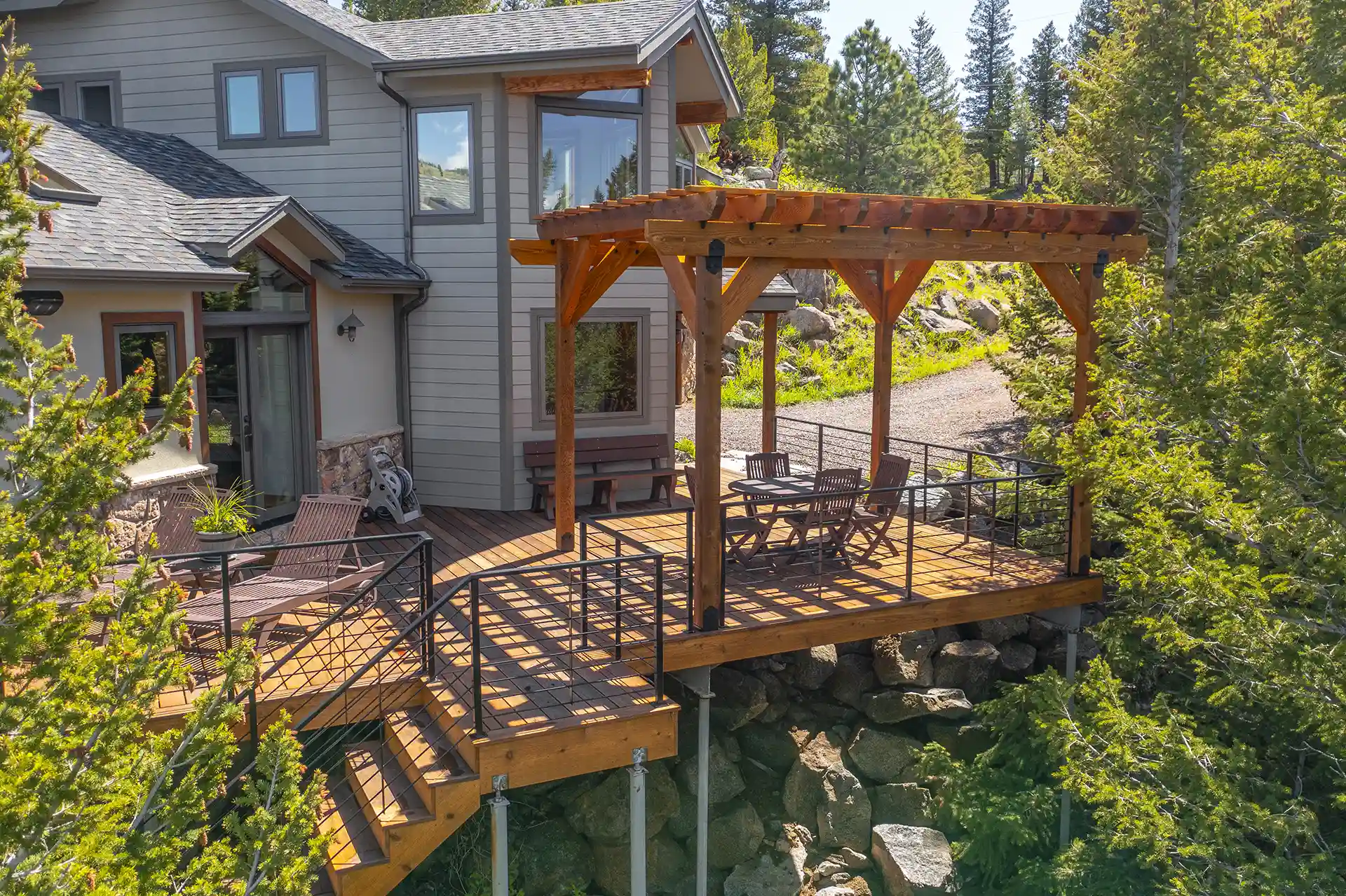An outdoor deck with a wooden pergola, metal railings, and a seating area featuring a table and chairs.
