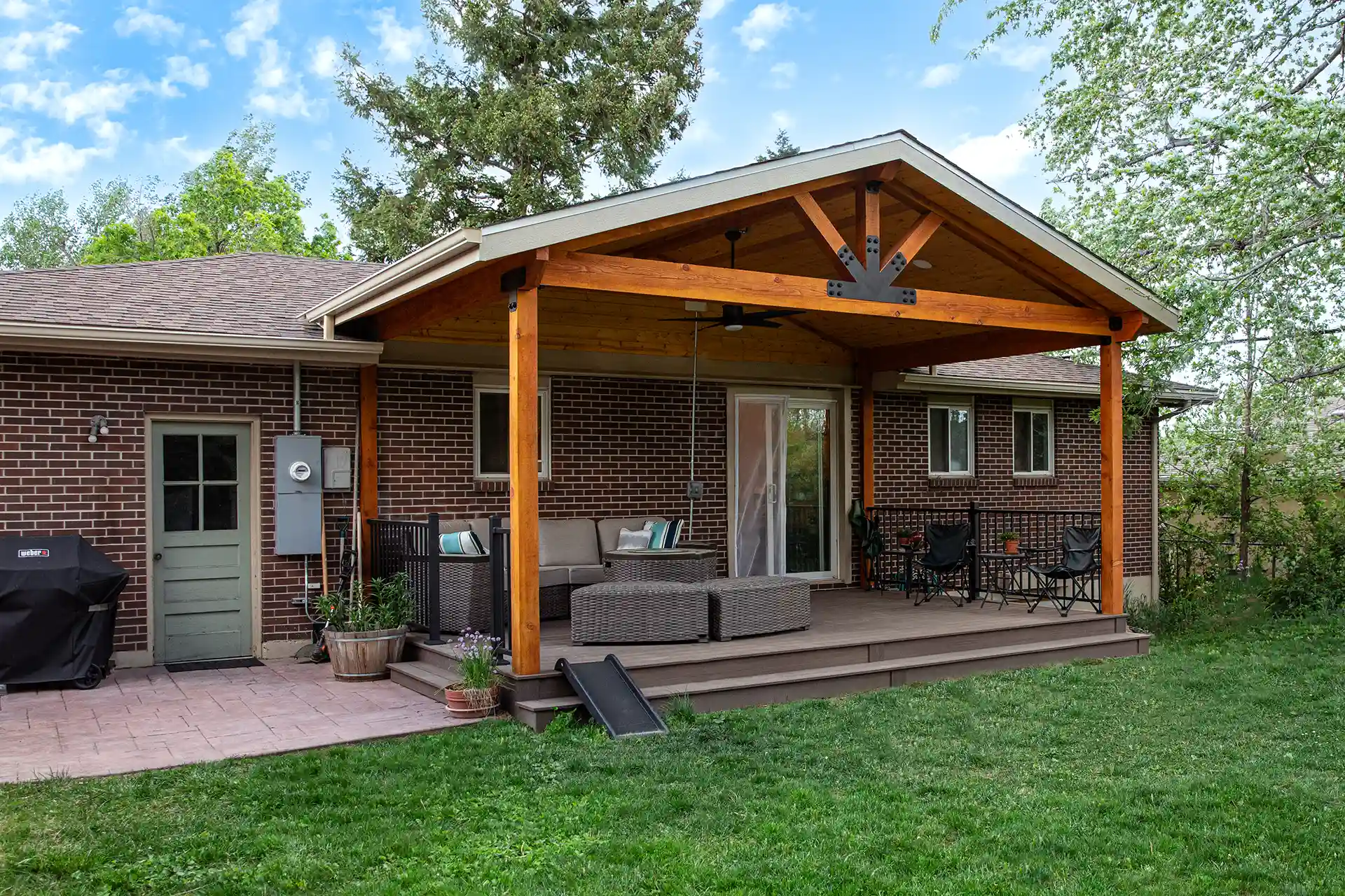 Backyard deck with wooden patio cover, outdoor seating, and ceiling fan attached to a brick house. 