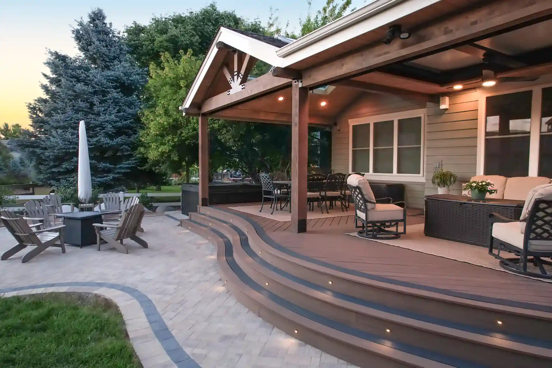 Multi-level composite deck with integrated lighting, a covered seating area, and an adjacent paver patio with a fire pit. 