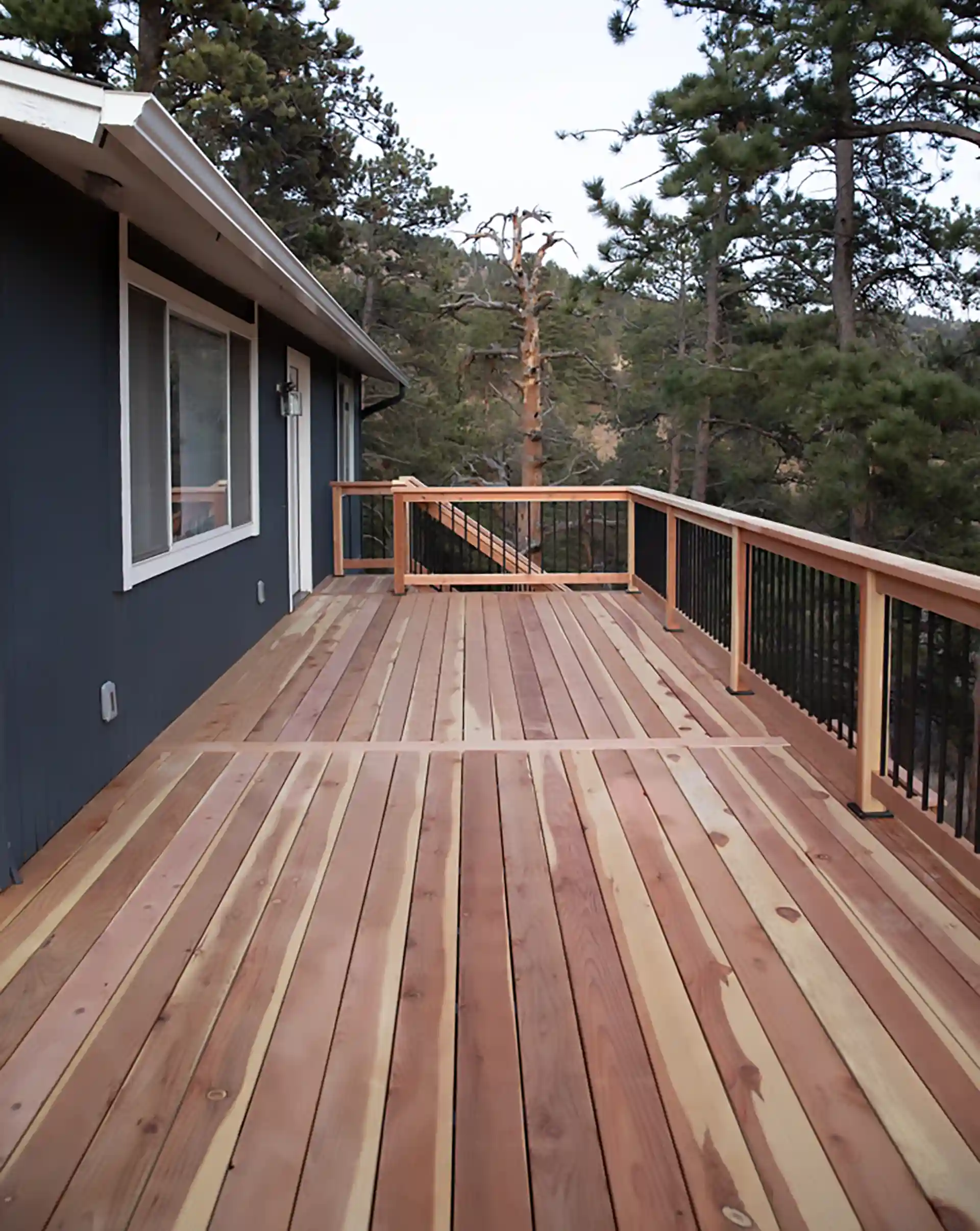 Spacious natural wood deck with horizontal railing, set against a forested mountain backdrop. 